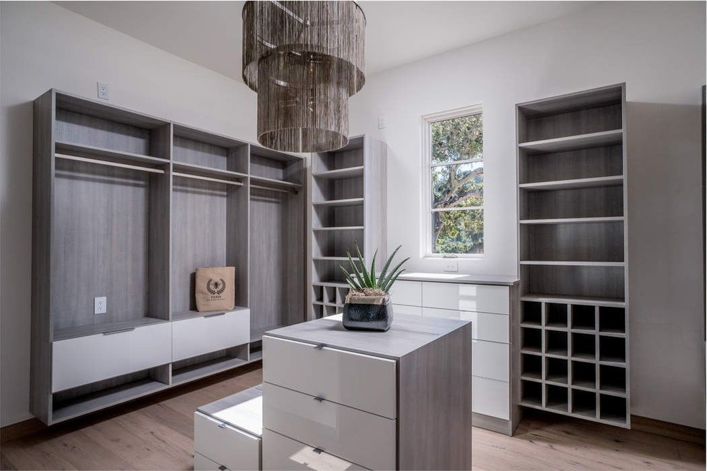 Mid-sized contemporary gender-neutral walk-in wardrobe in Other with flat-panel cabinets, white cabinets, light hardwood floors and beige floor.
