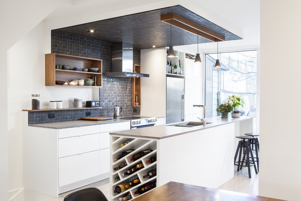 Contemporary galley open plan kitchen in Toronto with a double-bowl sink, flat-panel cabinets, white cabinets, black splashback, mosaic tile splashback, stainless steel appliances and with island.