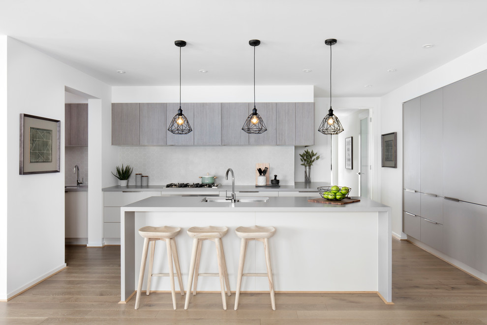Photo of a contemporary l-shaped kitchen in Geelong with an undermount sink, flat-panel cabinets, grey cabinets, light hardwood floors, with island and grey benchtop.