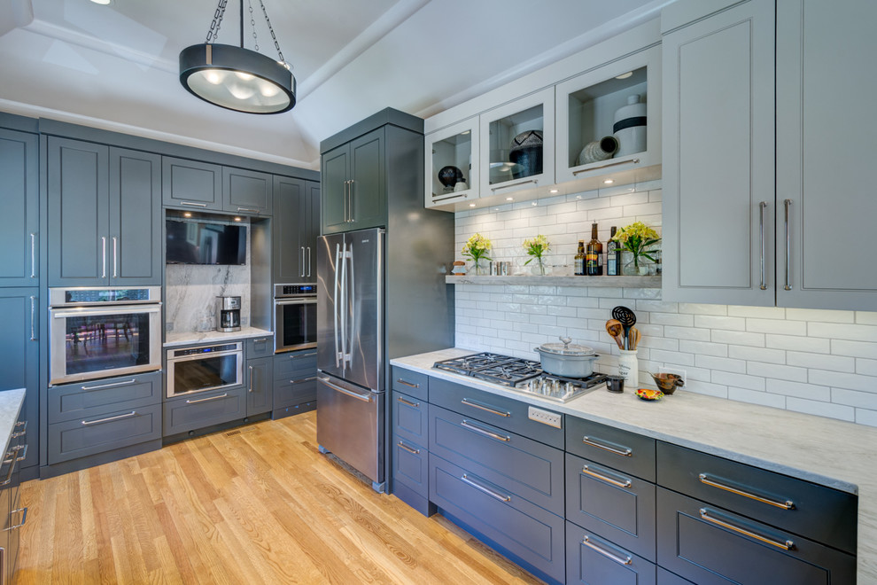 This is an example of a large contemporary u-shaped separate kitchen in Atlanta with an undermount sink, raised-panel cabinets, grey cabinets, quartzite benchtops, white splashback, subway tile splashback, stainless steel appliances, light hardwood floors, a peninsula, brown floor and white benchtop.