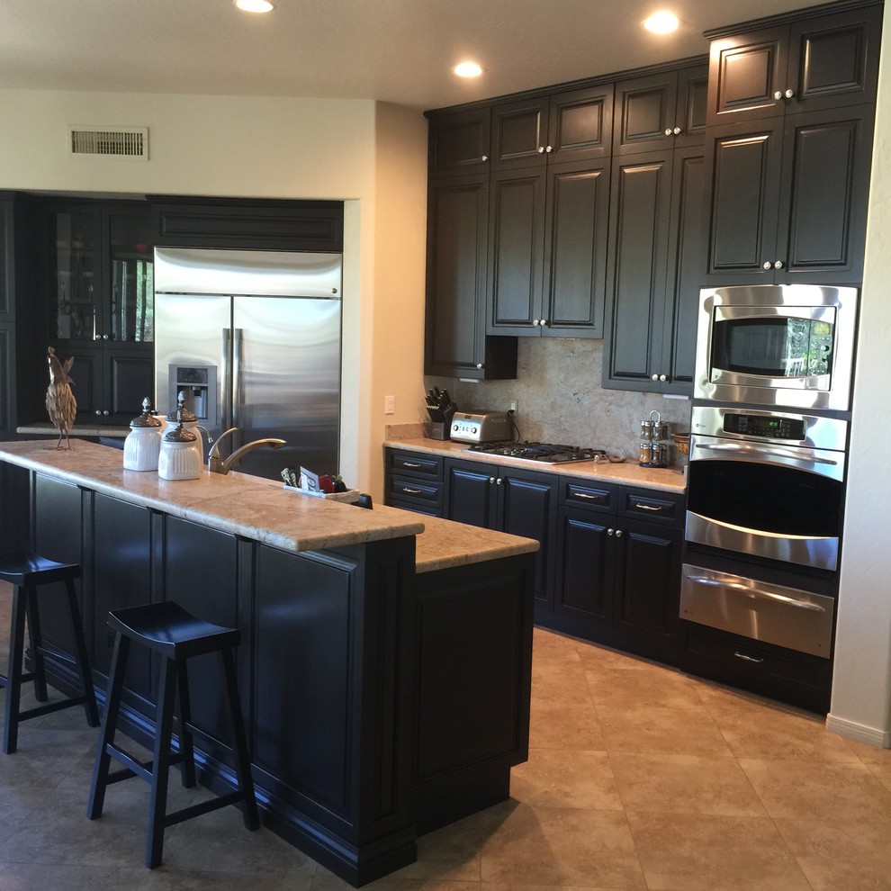 Inspiration for a mid-sized transitional l-shaped porcelain tile and beige floor open concept kitchen remodel in Phoenix with an undermount sink, raised-panel cabinets, black cabinets, granite countertops, beige backsplash, stone slab backsplash, stainless steel appliances and an island