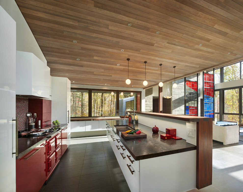 This is an example of a contemporary galley open plan kitchen in Philadelphia with a double-bowl sink, flat-panel cabinets, red cabinets, red splashback, mosaic tile splashback, coloured appliances, with island and grey floor.