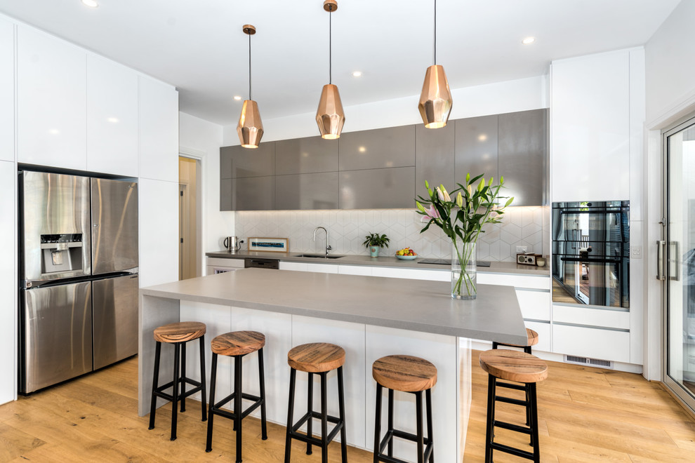 Design ideas for a large contemporary l-shaped open plan kitchen in Melbourne with an undermount sink, flat-panel cabinets, white cabinets, white splashback, stainless steel appliances, medium hardwood floors, with island and brown floor.