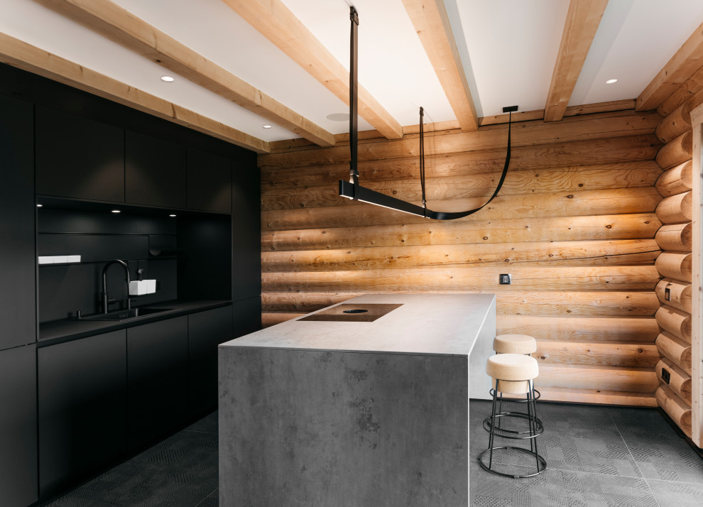 This is an example of a mid-sized contemporary open plan kitchen in Frankfurt with a drop-in sink, flat-panel cabinets, black cabinets, concrete benchtops, black splashback, black appliances, ceramic floors, with island, black floor, black benchtop and exposed beam.