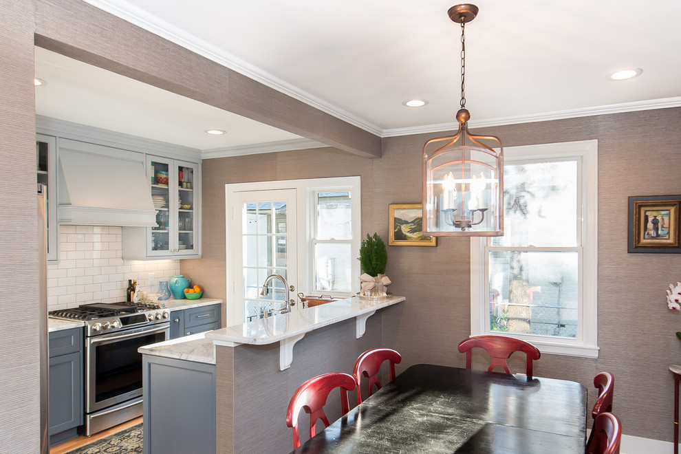Photo of a contemporary single-wall eat-in kitchen in Charleston with a farmhouse sink, white cabinets, white splashback, subway tile splashback, stainless steel appliances, light hardwood floors and a peninsula.
