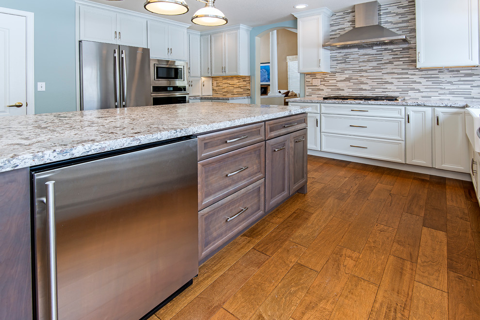 Enclosed kitchen - large transitional medium tone wood floor enclosed kitchen idea with a farmhouse sink, recessed-panel cabinets, white cabinets, granite countertops, multicolored backsplash, matchstick tile backsplash, stainless steel appliances and an island