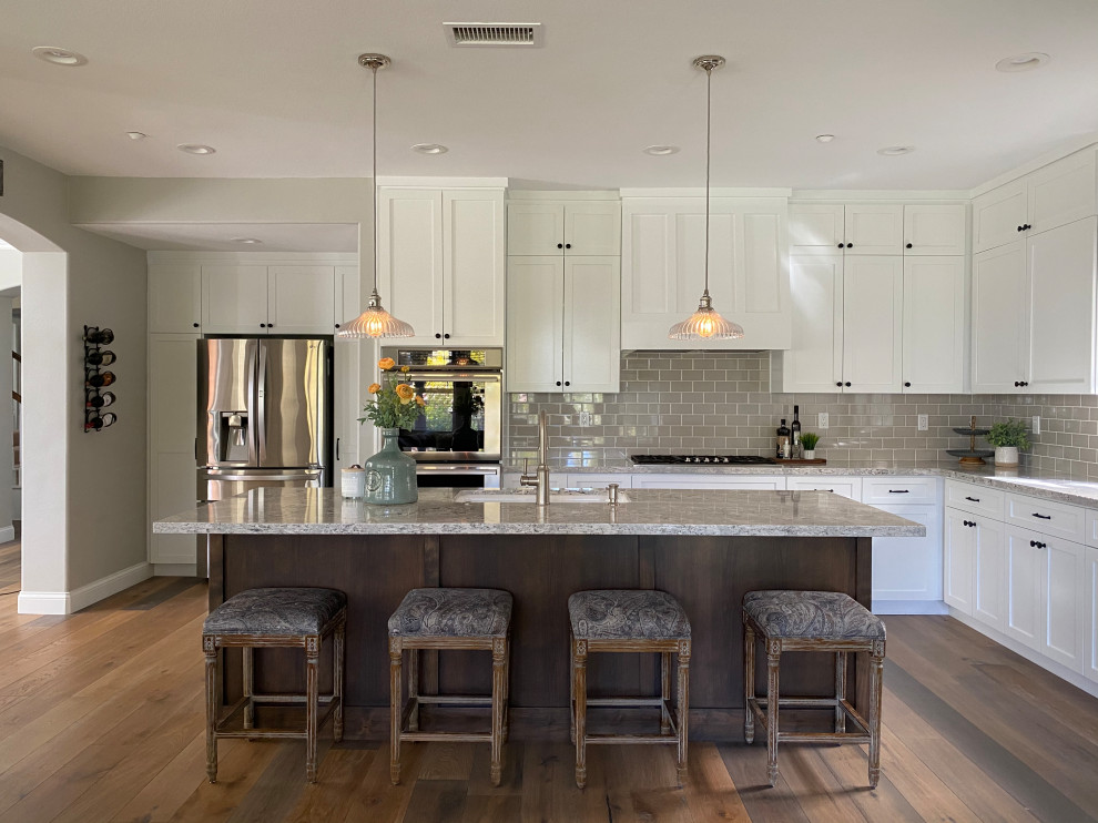 Inspiration for a large transitional l-shaped medium tone wood floor and brown floor kitchen remodel in San Luis Obispo with an undermount sink, shaker cabinets, white cabinets, gray backsplash, subway tile backsplash, stainless steel appliances, an island and gray countertops