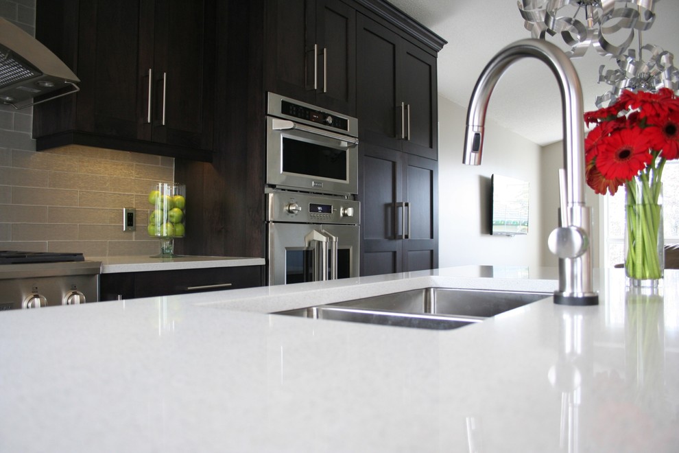 Example of a mid-sized transitional l-shaped dark wood floor open concept kitchen design in Calgary with a triple-bowl sink, shaker cabinets, dark wood cabinets, quartz countertops, gray backsplash, glass tile backsplash, stainless steel appliances and an island