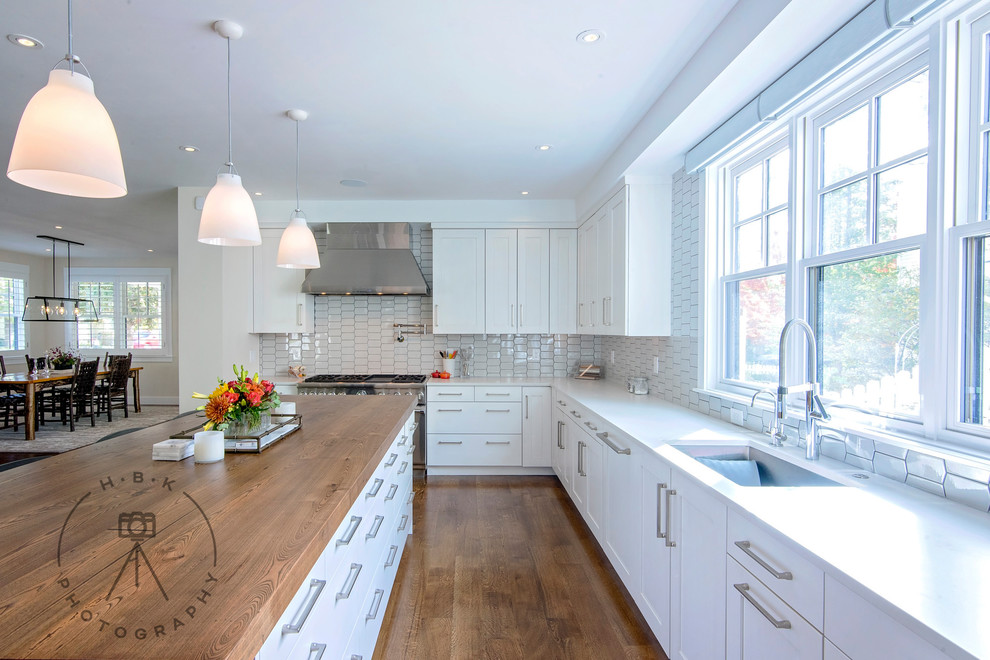 Inspiration for a large single-wall medium tone wood floor and brown floor open concept kitchen remodel with an undermount sink, recessed-panel cabinets, white cabinets, wood countertops, white backsplash, ceramic backsplash, stainless steel appliances, an island and brown countertops