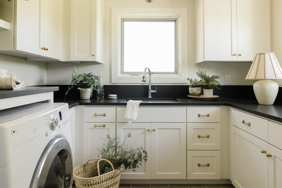 Photo of a mid-sized traditional u-shaped dedicated laundry room in Other with an undermount sink, recessed-panel cabinets, white cabinets, quartz benchtops, black splashback, engineered quartz splashback, white walls, ceramic floors, a side-by-side washer and dryer, grey floor and black benchtop.