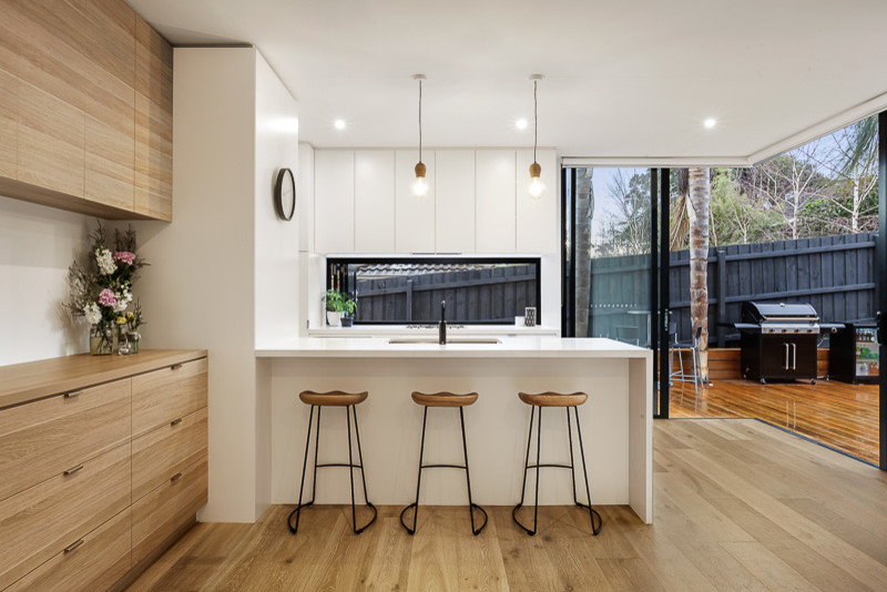 This is an example of a small scandinavian single-wall eat-in kitchen in Melbourne with an undermount sink, flat-panel cabinets, white cabinets, quartz benchtops, stainless steel appliances, light hardwood floors, window splashback and a peninsula.