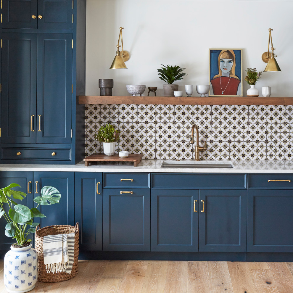 Cette photo montre une arrière-cuisine chic avec un placard avec porte à panneau encastré, des portes de placard bleues, une crédence blanche, parquet clair, un sol marron et un plan de travail blanc.