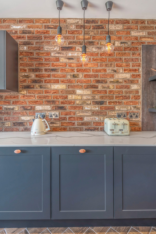 Inspiration for an industrial single-wall kitchen in Berkshire with shaker cabinets, blue cabinets, brick splashback, black appliances, with island and brown floor.