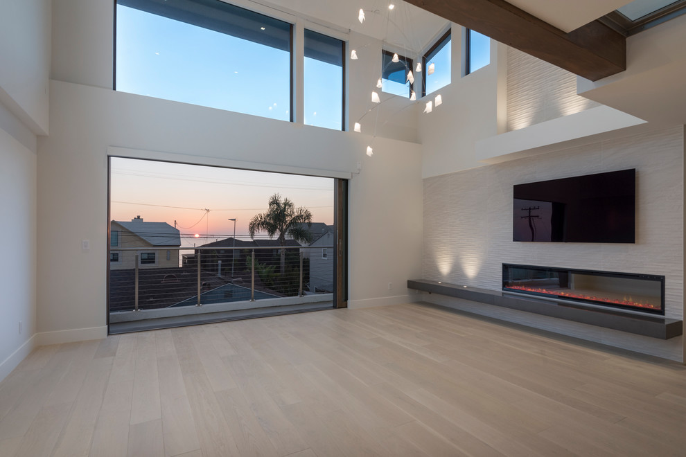 Large modern open concept family room in San Diego with white walls, light hardwood floors, a hanging fireplace, a tile fireplace surround and a wall-mounted tv.