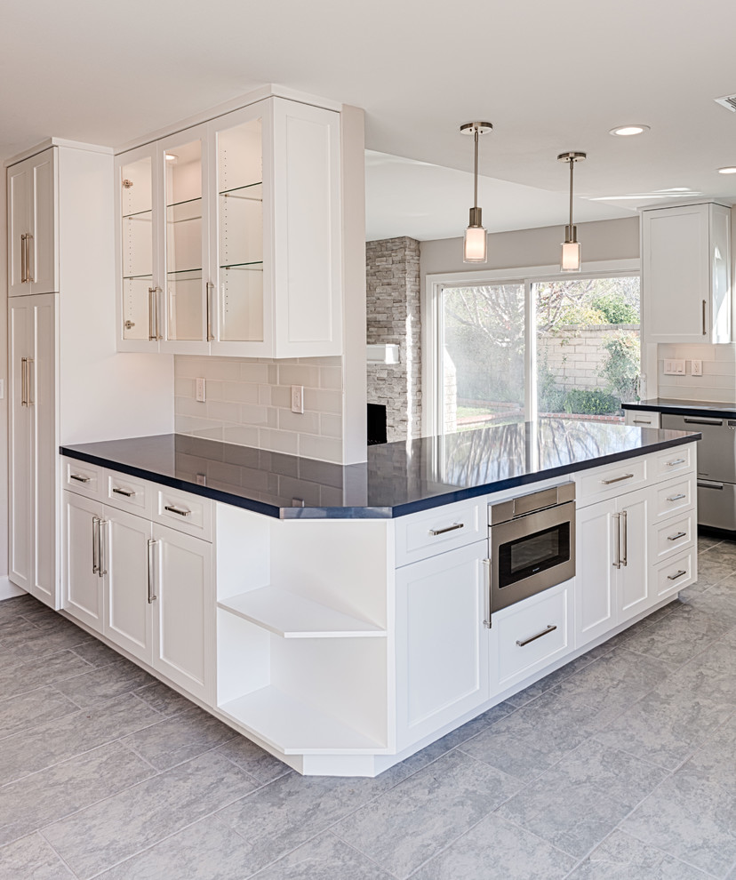 This is an example of a large arts and crafts l-shaped eat-in kitchen in Los Angeles with an undermount sink, shaker cabinets, white cabinets, quartz benchtops, white splashback, subway tile splashback, stainless steel appliances, porcelain floors, a peninsula, grey floor and black benchtop.
