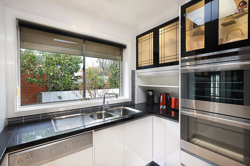 Inspiration for a mid-sized u-shaped separate kitchen in Melbourne with a double-bowl sink, flat-panel cabinets, black cabinets, quartz benchtops, pink splashback, glass sheet splashback, stainless steel appliances, ceramic floors and a peninsula.