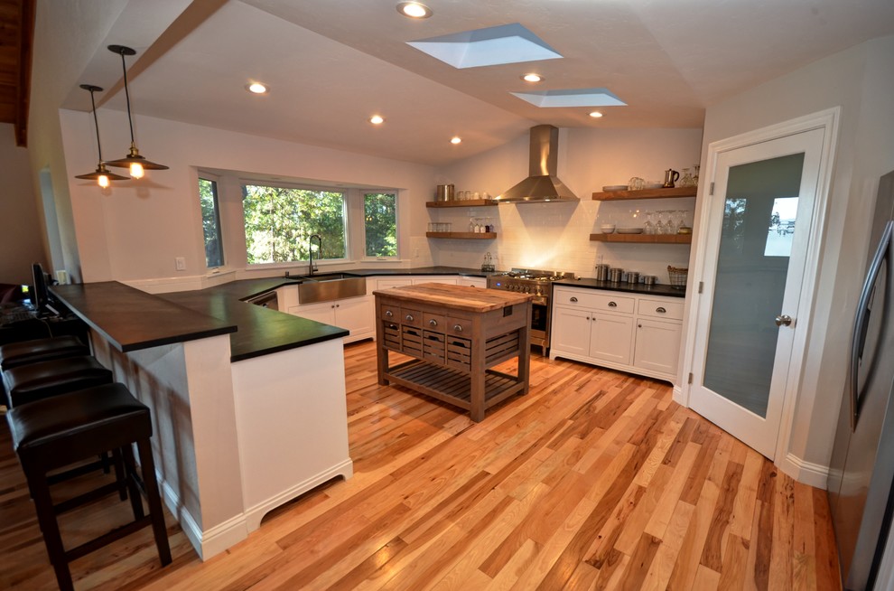 Design ideas for an arts and crafts u-shaped open plan kitchen in Sacramento with shaker cabinets, white cabinets, solid surface benchtops, with island, a farmhouse sink, white splashback, subway tile splashback, stainless steel appliances and light hardwood floors.