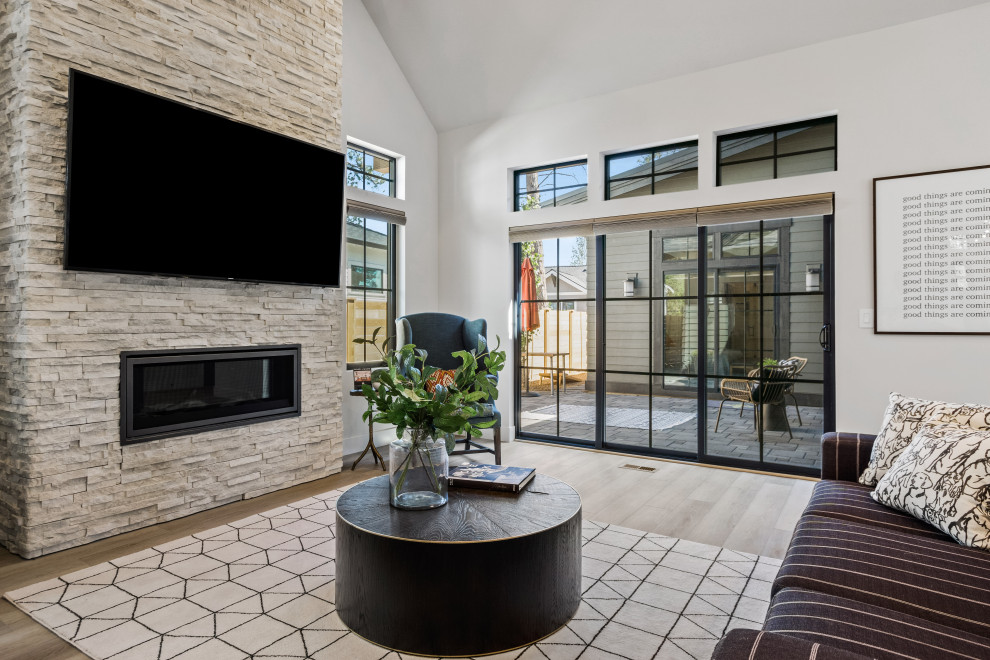 This is an example of a medium sized contemporary open plan living room in Other with white walls, light hardwood flooring, a standard fireplace, a stacked stone fireplace surround, a wall mounted tv, brown floors and a vaulted ceiling.