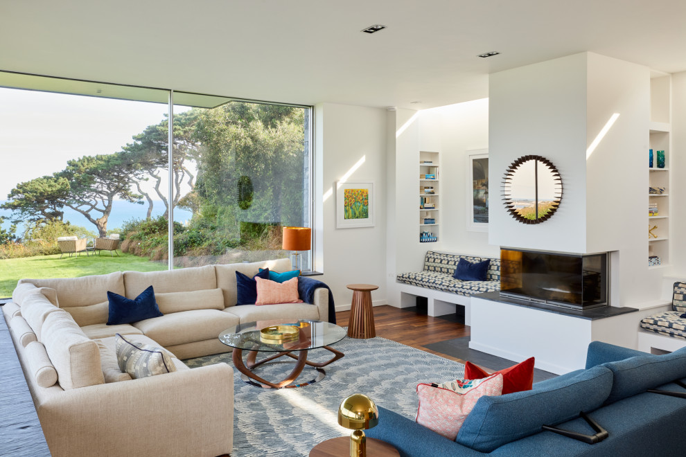 Expansive contemporary open plan living room in Channel Islands with white walls, dark hardwood flooring, a plastered fireplace surround, a ribbon fireplace and brown floors.