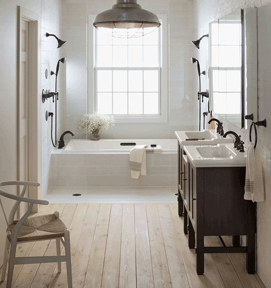 Photo of a mid-sized country master bathroom in Chicago with recessed-panel cabinets, dark wood cabinets, a drop-in tub, a curbless shower, a one-piece toilet, beige tile, porcelain tile, beige walls, light hardwood floors, a console sink, granite benchtops and beige floor.