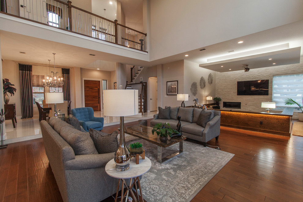 This is an example of a large contemporary open concept family room in Dallas with grey walls, medium hardwood floors, a ribbon fireplace, a stone fireplace surround and a wall-mounted tv.