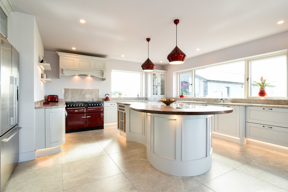 This is an example of a transitional u-shaped open plan kitchen in Other with recessed-panel cabinets, white cabinets, marble benchtops, marble splashback, with island and beige floor.