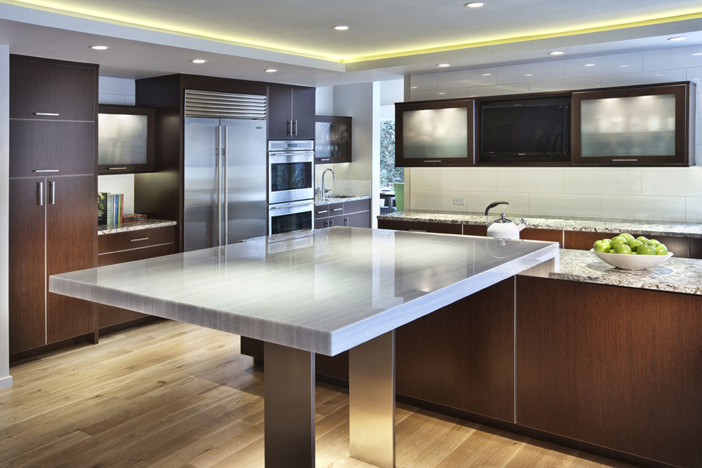 Inspiration for a contemporary l-shaped eat-in kitchen in Denver with an undermount sink, flat-panel cabinets, dark wood cabinets, granite benchtops, white splashback, subway tile splashback and stainless steel appliances.