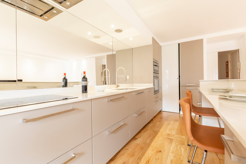 Design ideas for a mid-sized contemporary galley eat-in kitchen in Nice with an undermount sink, flat-panel cabinets, beige cabinets, marble benchtops, white splashback, mirror splashback, panelled appliances, medium hardwood floors, with island, beige floor and beige benchtop.