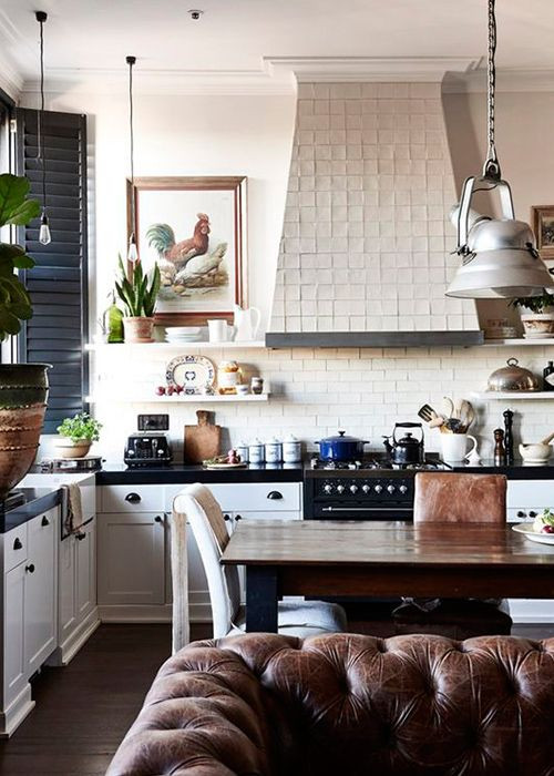 Inspiration for a mid-sized eclectic l-shaped open plan kitchen in Columbus with a farmhouse sink, shaker cabinets, white cabinets, quartzite benchtops, white splashback, porcelain splashback, black appliances, dark hardwood floors, brown floor and black benchtop.
