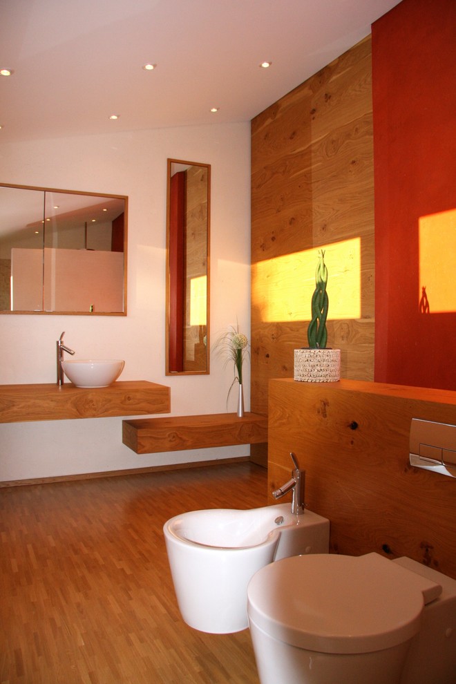 This is an example of a mid-sized asian 3/4 bathroom in Munich with beaded inset cabinets, beige cabinets, a wall-mount toilet, red walls, light hardwood floors, a vessel sink, wood benchtops and beige floor.