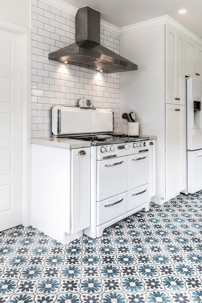 Mid-sized country galley separate kitchen in Los Angeles with white cabinets, marble benchtops, white splashback, ceramic splashback, white appliances, cement tiles, no island, multi-coloured floor, a farmhouse sink and shaker cabinets.