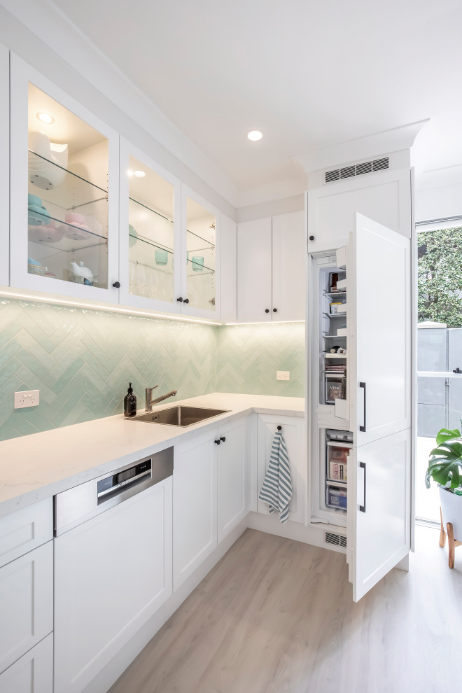 Photo of a small traditional u-shaped eat-in kitchen in Sydney with a drop-in sink, shaker cabinets, white cabinets, quartz benchtops, green splashback, porcelain splashback, stainless steel appliances, vinyl floors, grey floor and white benchtop.