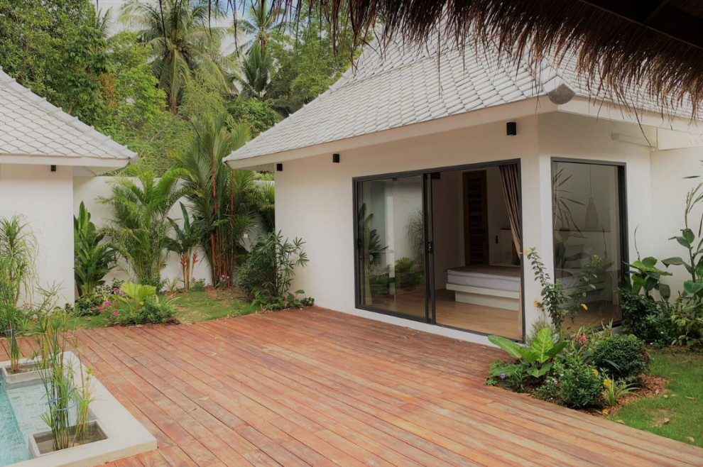 Ejemplo de terraza planta baja tropical grande en patio y anexo de casas con jardín vertical y barandilla de madera