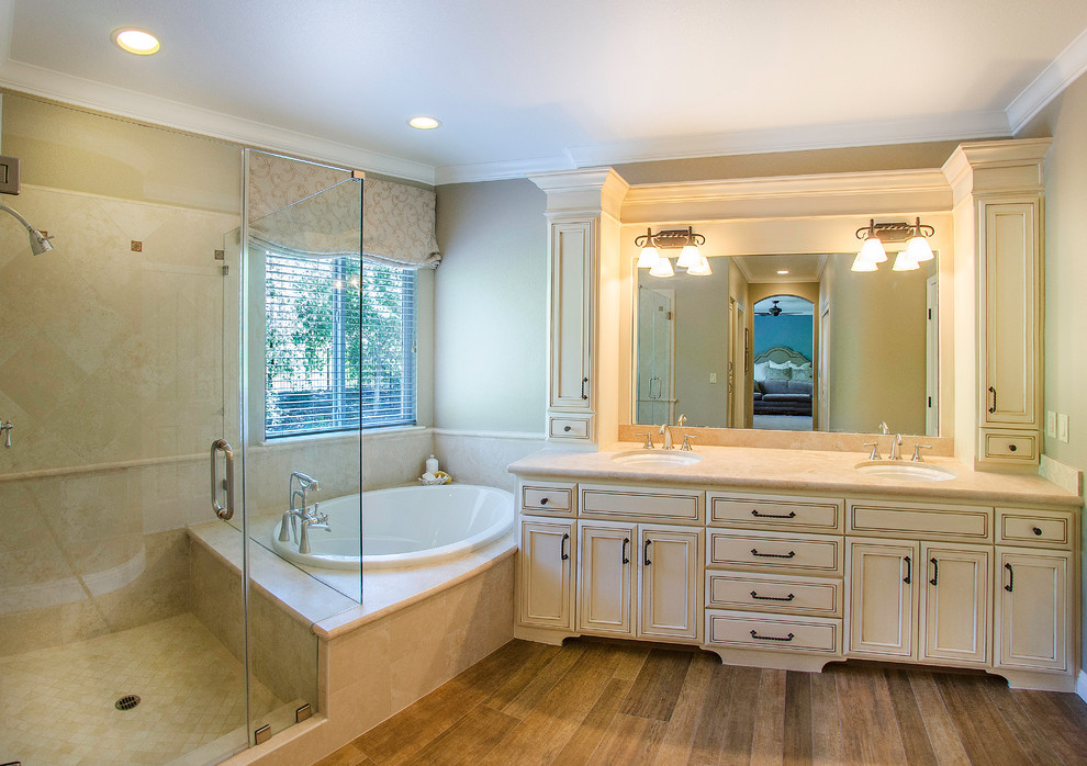 This is an example of a mid-sized traditional bathroom in Sacramento with an undermount sink, a drop-in tub, a corner shower, recessed-panel cabinets, white cabinets, limestone benchtops, beige tile, porcelain tile, beige walls and porcelain floors.
