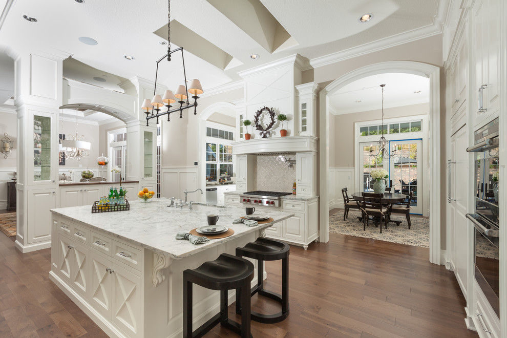 This is an example of a traditional u-shaped eat-in kitchen in Portland with an undermount sink, raised-panel cabinets, white cabinets, beige splashback, stainless steel appliances and dark hardwood floors.