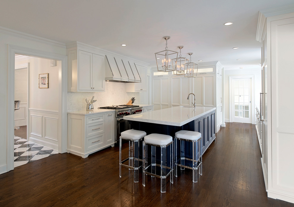 Inredning av ett klassiskt mellanstort vit vitt kök, med luckor med infälld panel, vita skåp, bänkskiva i kvartsit, vitt stänkskydd, rostfria vitvaror, mörkt trägolv, en köksö och brunt golv