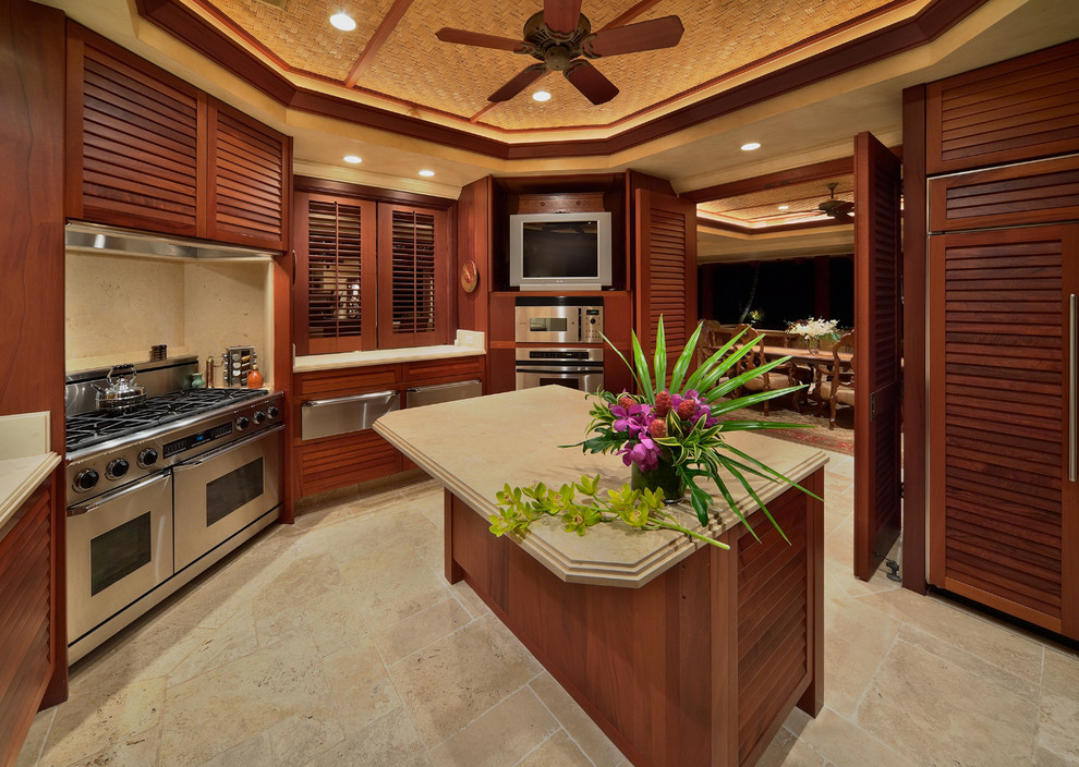 Photo of a large tropical kitchen in Hawaii with louvered cabinets, dark wood cabinets, panelled appliances, travertine floors, with island and beige floor.