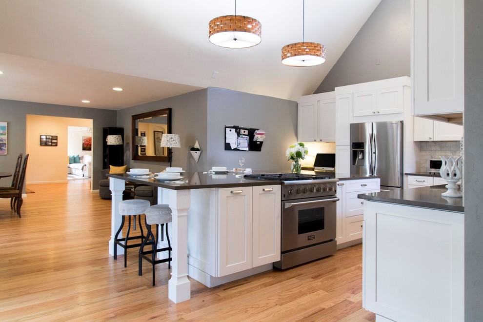 Inspiration for an expansive transitional l-shaped eat-in kitchen in Denver with a farmhouse sink, shaker cabinets, white cabinets, quartz benchtops, white splashback, stone tile splashback, stainless steel appliances, light hardwood floors and with island.