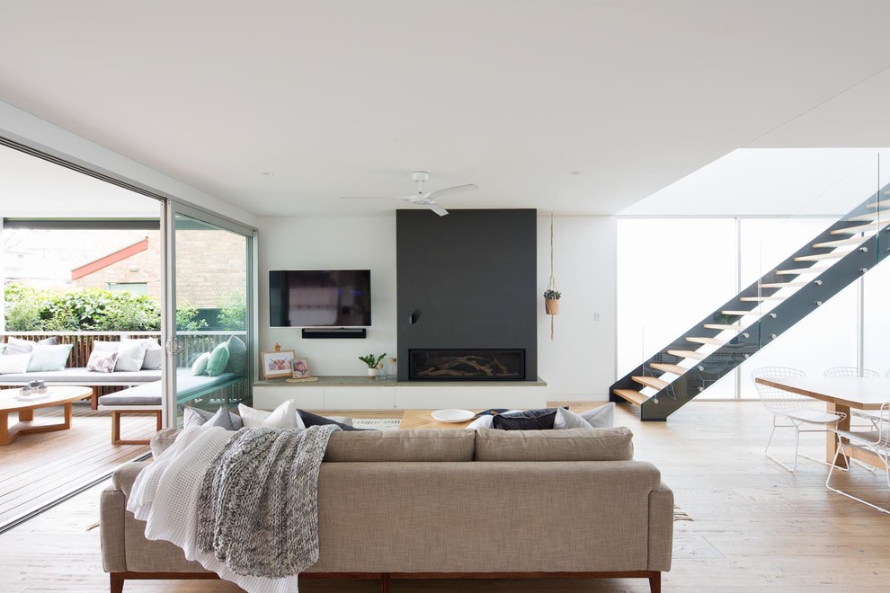 This is an example of a large contemporary open concept living room in Sydney with white walls, medium hardwood floors, a standard fireplace, a concrete fireplace surround, a wall-mounted tv and brown floor.