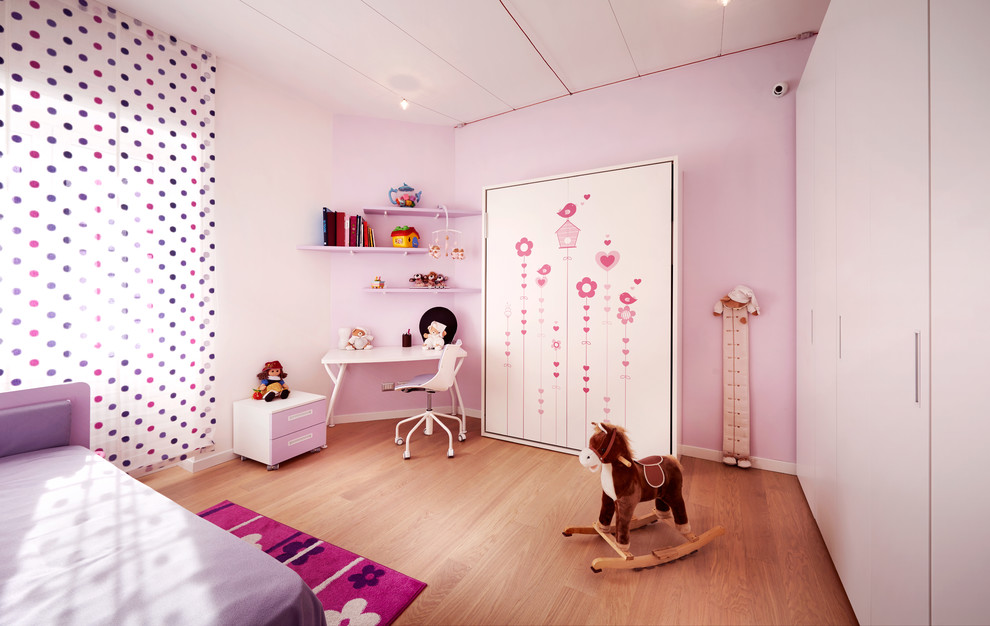 This is an example of a mid-sized modern kids' bedroom for kids 4-10 years old and girls in Rome with pink walls, medium hardwood floors and brown floor.