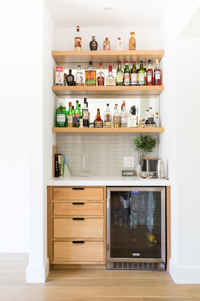 Contemporary single-wall home bar in Los Angeles with flat-panel cabinets, medium wood cabinets, medium hardwood floors, brown floor and white benchtop.