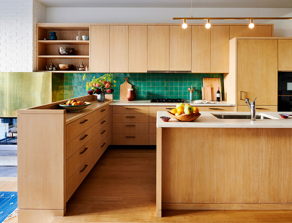 Design ideas for a midcentury u-shaped kitchen in New York with a drop-in sink, flat-panel cabinets, light wood cabinets, green splashback, light hardwood floors, with island and brown floor.