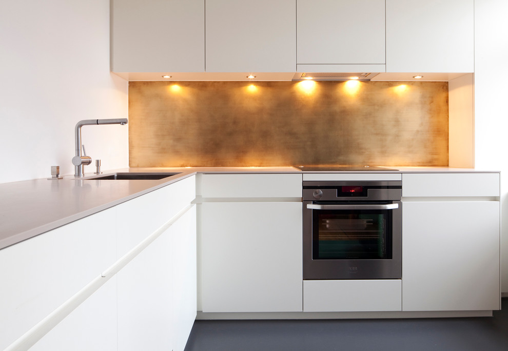 Contemporary l-shaped open plan kitchen in Munich with an undermount sink, flat-panel cabinets, white cabinets, solid surface benchtops, metallic splashback, stainless steel appliances and linoleum floors.