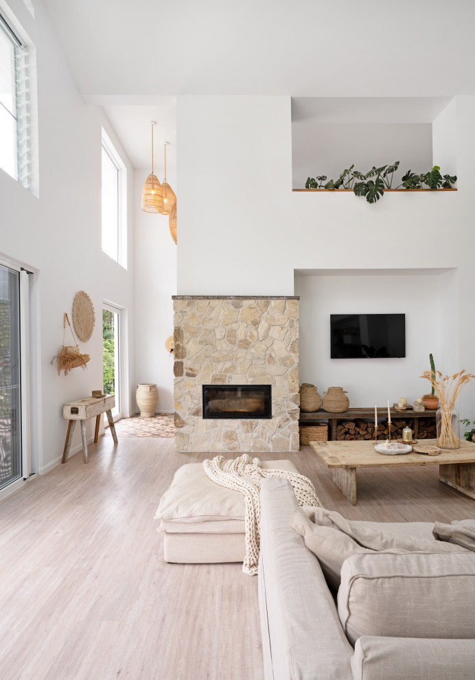 На фото: открытая гостиная комната в средиземноморском стиле с белыми стенами, полом из винила, фасадом камина из камня, телевизором на стене, бежевым полом и сводчатым потолком с