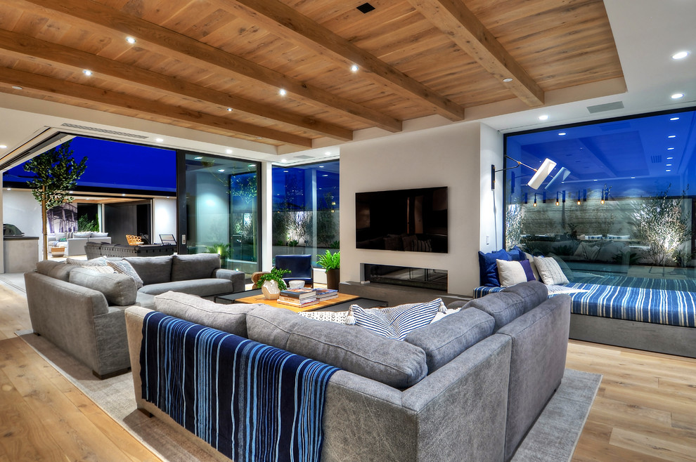 This is an example of an expansive modern open concept family room in Orange County with grey walls, medium hardwood floors, a ribbon fireplace, a concrete fireplace surround and a wall-mounted tv.