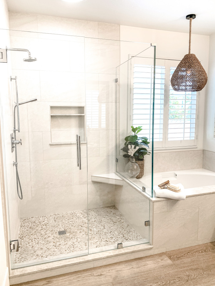 This is an example of a mid-sized beach style master bathroom in Orange County with shaker cabinets, white cabinets, an undermount tub, a corner shower, beige tile, porcelain tile, white walls, light hardwood floors, a drop-in sink, quartzite benchtops, a hinged shower door, beige benchtops, a shower seat, a double vanity and a built-in vanity.
