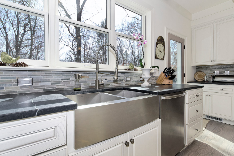 Transitional u-shaped open concept kitchen photo with a farmhouse sink, raised-panel cabinets, white cabinets, soapstone countertops, multicolored backsplash and stainless steel appliances
