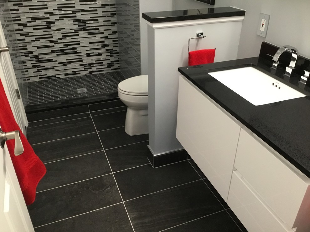 This is an example of a small contemporary 3/4 bathroom in Detroit with flat-panel cabinets, white cabinets, an alcove shower, a one-piece toilet, black and white tile, glass tile, grey walls, porcelain floors, an undermount sink, granite benchtops, black floor and a hinged shower door.