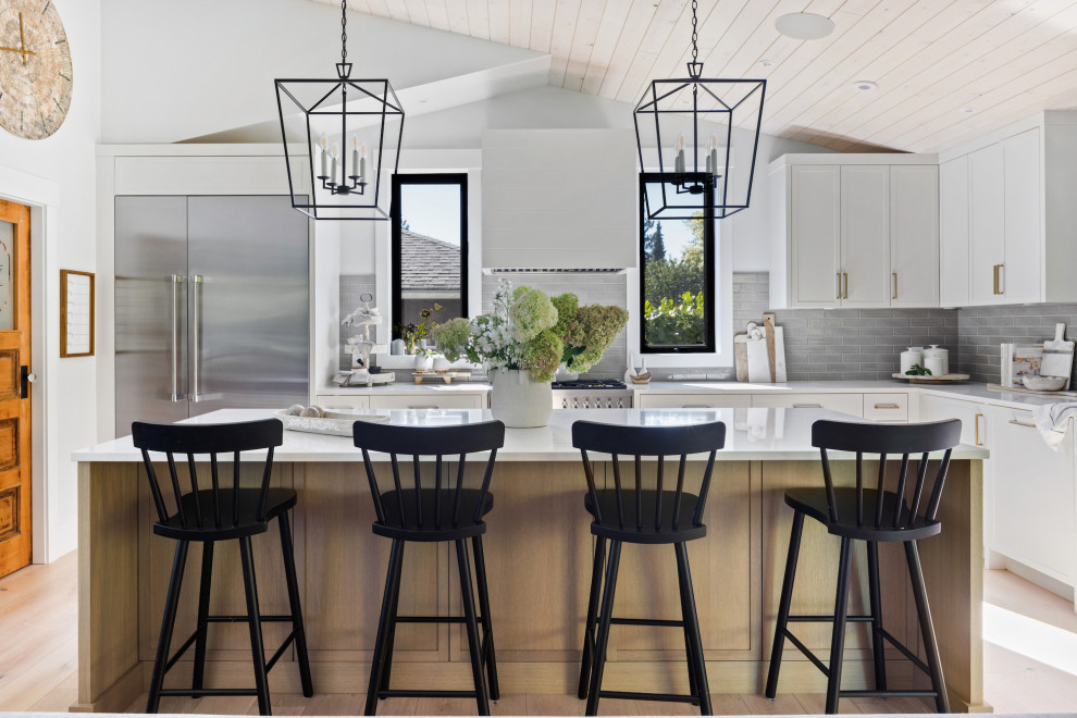 Mid-sized beach style u-shaped light wood floor and shiplap ceiling open concept kitchen photo in Vancouver with a farmhouse sink, recessed-panel cabinets, white cabinets, granite countertops, gray backsplash, ceramic backsplash, stainless steel appliances, an island and white countertops