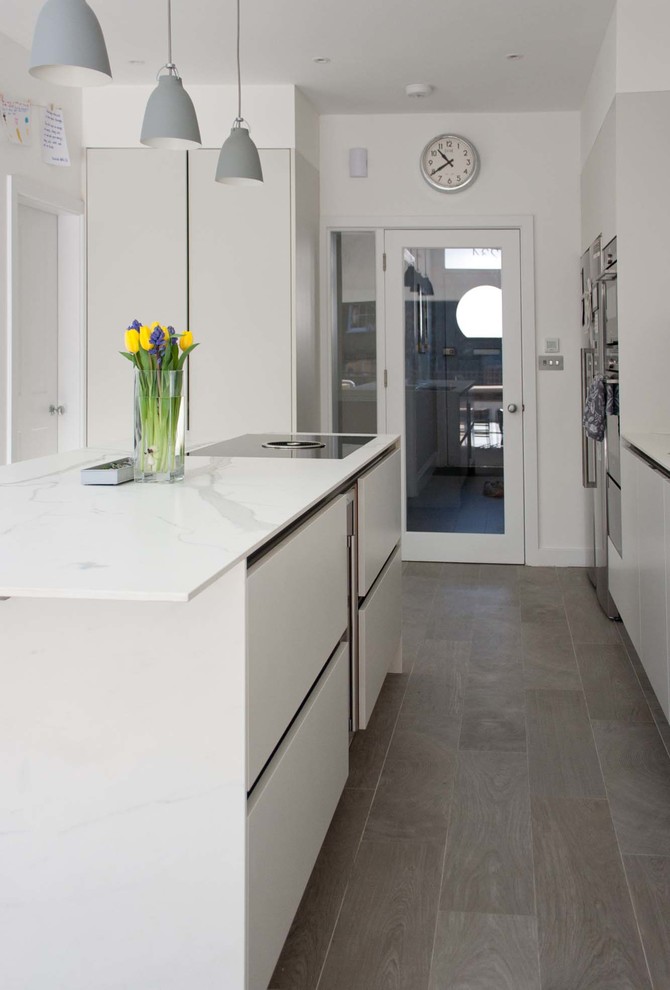 This is an example of a mid-sized contemporary single-wall eat-in kitchen in London with a single-bowl sink, flat-panel cabinets, white cabinets, limestone benchtops, white splashback, black appliances, porcelain floors, with island and grey floor.